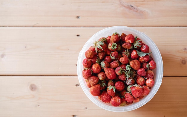 A bucket of strawberries on a wooden floor top view victoria harvest in a bucket