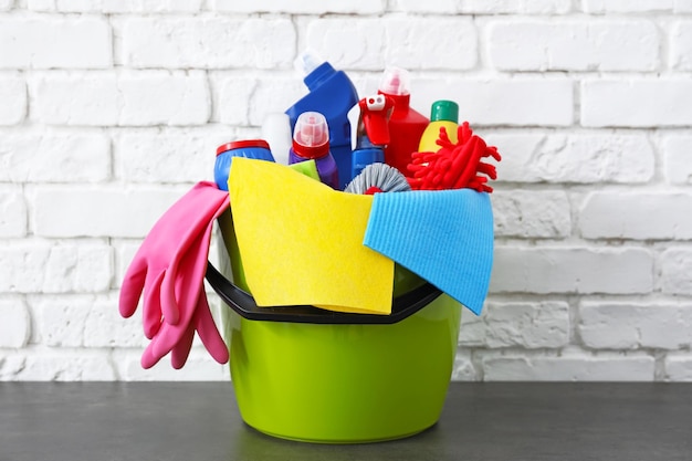 Bucket with cleaning supplies and tools on table near brick wall