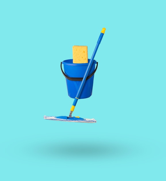 A bucket with a large sponge and a mop levitating on a light background The concept of cleaning the premises