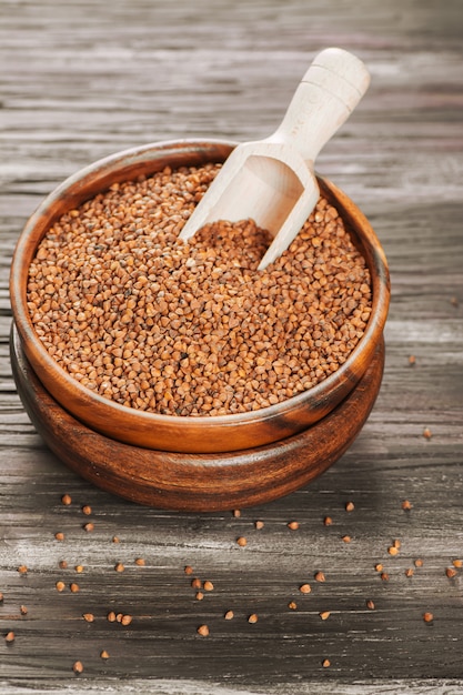 Buckwheat groats in a bowl and wooden scoop with buckwheat on grunge background