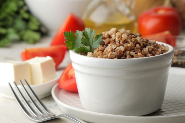 Buckwheat. Porridge cereals with parsley in a white ceramic bowl and tomato on a bright table. breakfast, healthy food.