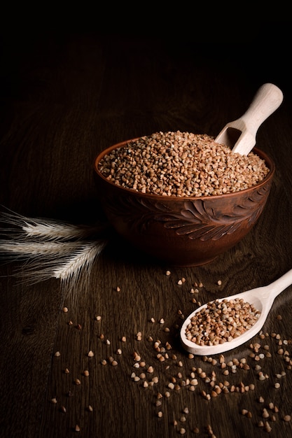 Buckwheat in a wooden bowl on a wooden table near the ears of wheat. wooden spoon with Buckwheat