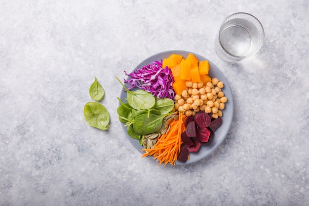 Buddha Bowl with  chickpea, beetroot, fresh spinach, pumpkin and purple cabbage, glass of water. Concept for  healthy vegetarian detox balanced  meal. Top view. Copy space.