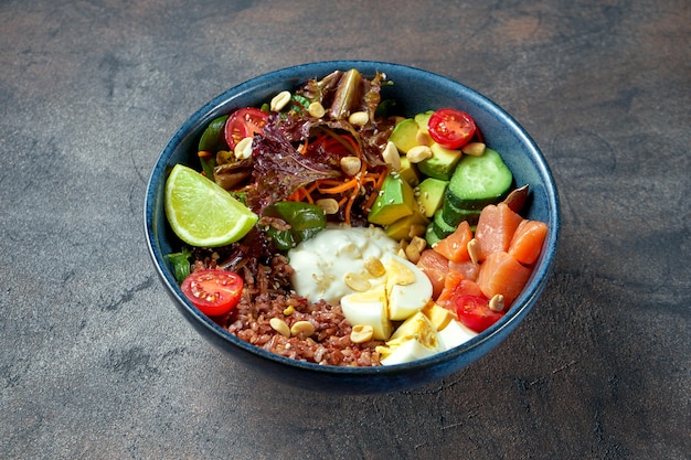 Buddha bowl with salmon, tomatoes, vegetables and wild rice, avocado and cucumbers in a blue plate.