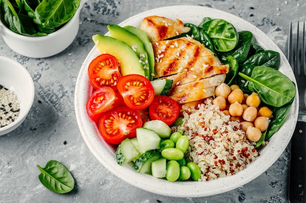 Buddha bowl with spinach salad quinoa roasted chickpeas grilled chicken avocado tomatoes cucumbers sesame seeds