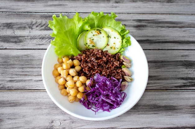 Buddha bowl with vegetables chickpeas red cabbage lettuce red rice zucchinipi stachios on wooden background