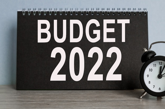 BUDGET 2022, alarm clock, BLACK notebook with text , on blue background, Time running away.