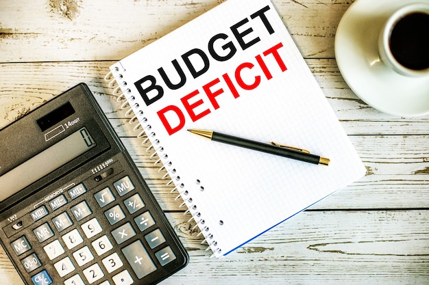 Photo budget deficit written on white paper near coffee and calculator on a light wooden table