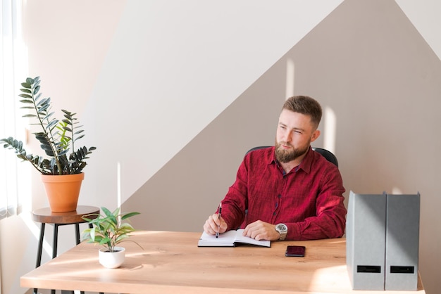 Budget planning Pensive bearded man writing in a notebook while sitting