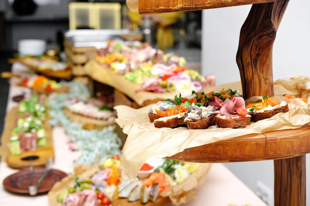 Buffet table with cold appetizers Meat and vegetable snacks are placed on wooden stands Stand with brusettas in the foreground