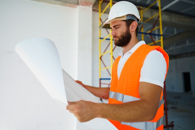 Builder or architect in hardhat supervising a project looking at blueprints