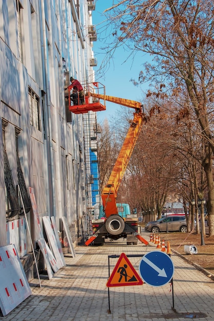 Builder in a crane basket repairs the coating of a metal structure on the wall of the facade