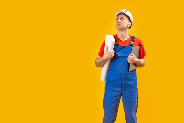 Builder or Man engineer in blue work suit wears safety helmet and holds drawings and documents looking up Isolated on yellow background Copy space