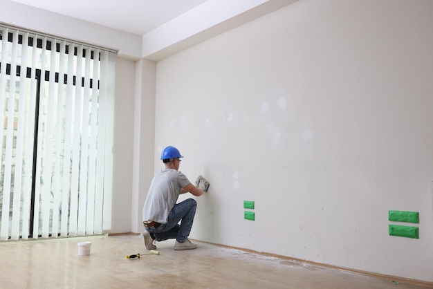 The builder putty a white wall in the room renovation of apartment a construction worker works