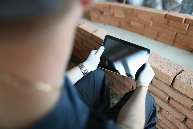 Builder stands in house under construction and holds tablet computer