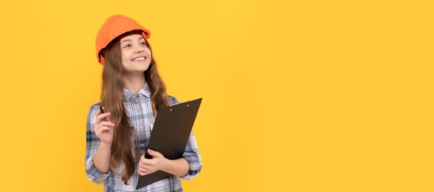 Builder teenager girl in helmet happy teen girl in helmet and checkered shirt making notes on clipboard inspector Child in hard hat horizontal poster design Banner header copy space