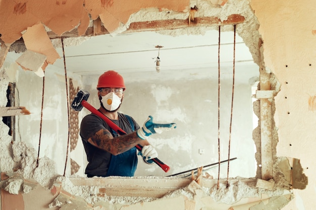 Builder with a hammer in his hands breaks the cement wall