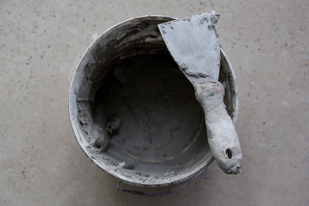 Builder work tool putty knife in gray putty on bucket