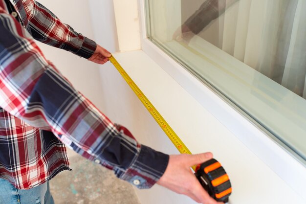 Photo builderrepairman measures the length of the installed window sill closeup