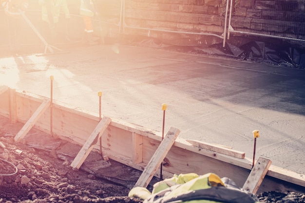 Builders pouring concrete slab and using vibrating poker to compact wet concrete