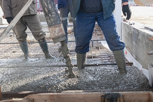 Builders workers pour concrete floor in industrial workshop Legs in boots in concrete Submission of concrete for pouring the floor Monolithic concrete works