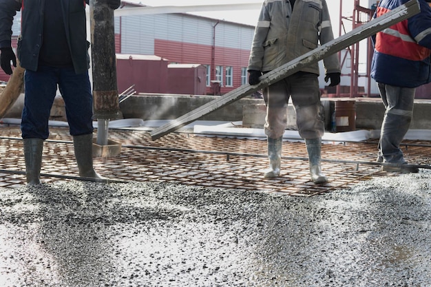 Builders workers pour concrete floor in industrial workshop Legs in boots in concrete Submission of concrete for pouring the floor Monolithic concrete works