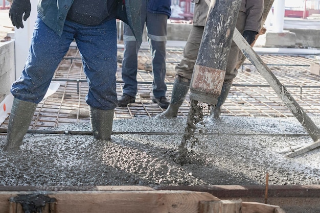 Builders workers pour concrete floor in industrial workshop Legs in boots in concrete Submission of concrete for pouring the floor Monolithic concrete works