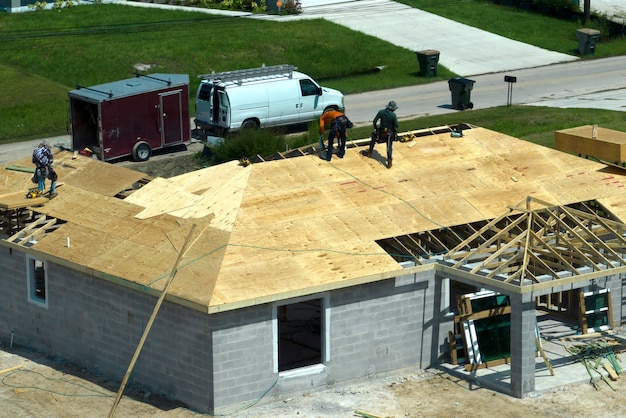 Builders working on roof construction of unfinished residential house with wooden frame structure in Florida suburban area Housing development concept