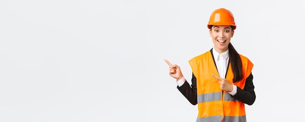 Building construction and industrial concept Smiling female engineer in helmet and reflective clothing showing way pointing upper left corner talking about constructing project white background