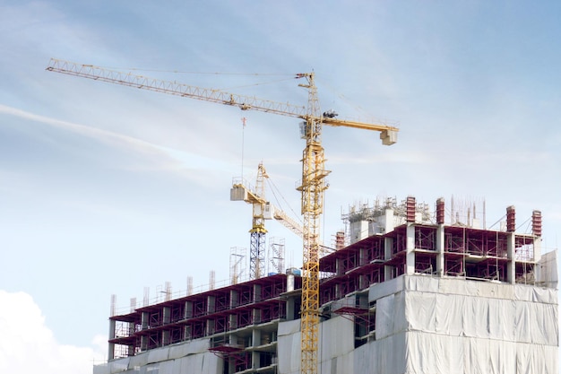 Building under construction with hoisting cranes working under the blue sky and silken cloud