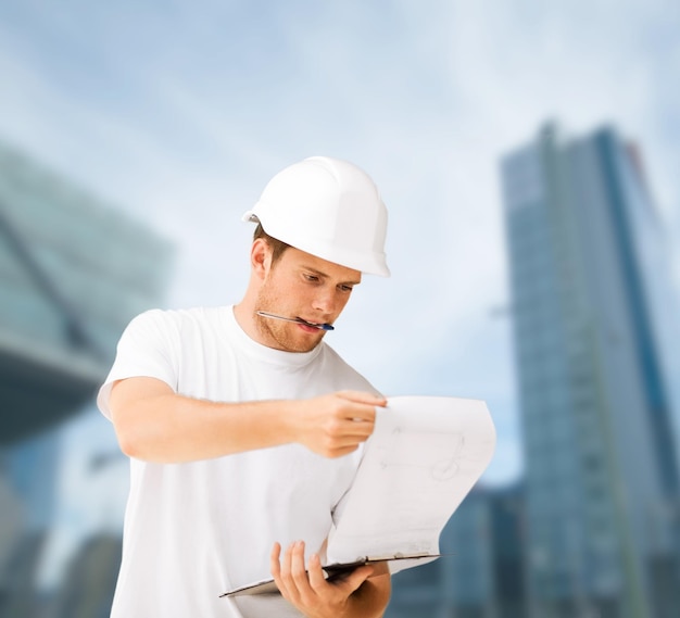 building, developing, consrtuction and architecture concept - male architect in helmet looking at blueprint