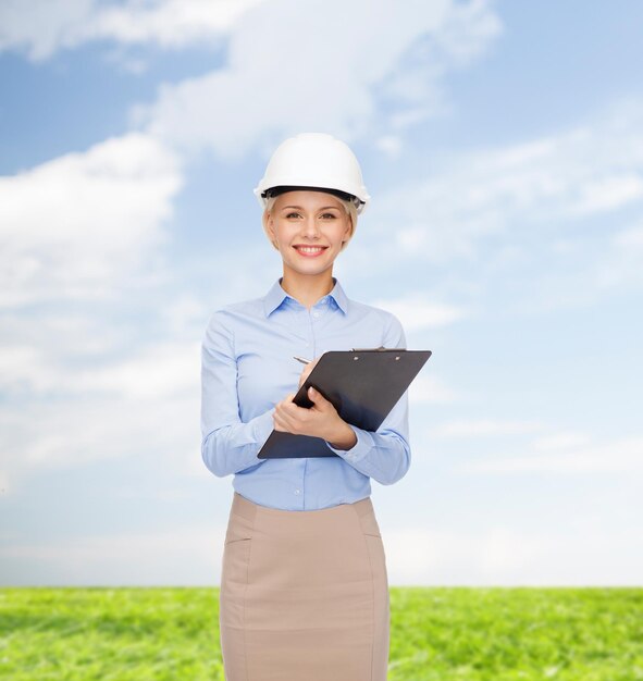 building, developing, construction and architecture concept - smiling businesswoman in white helmet with clipboard