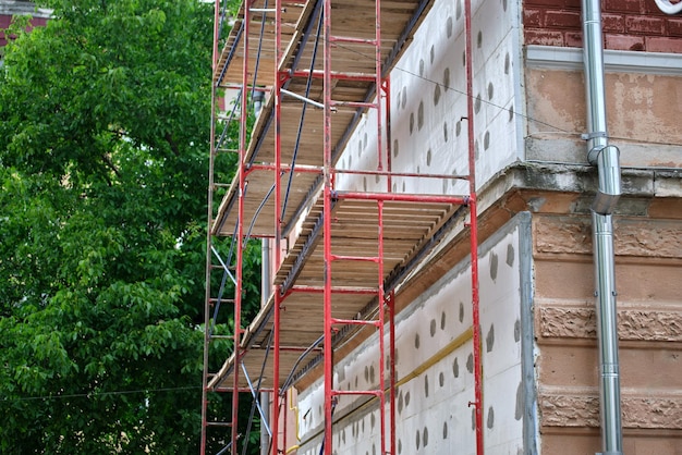 Building facade under renovation works with construction scaffolding frame Wall insulation with styrofoam sheets for energy efficient home