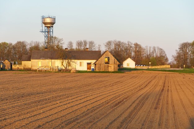 Photo the building of a livestock farm a water tower and a plowed field during sunset an agricultural field on the territory of an industrial complex farm shed land cultivation private small business