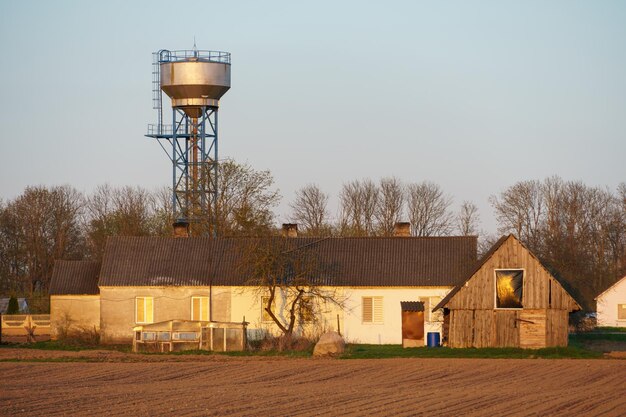 Photo the building of a livestock farm a water tower and a plowed field during sunset an agricultural field on the territory of an industrial complex farm shed land cultivation private small business