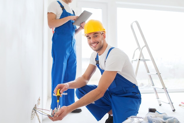 building, renovation, technology, electricity and people concept - two builders with tablet pc computer working with electricity indoors