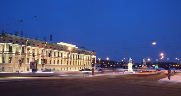 Buildings with glowing lights in winter and a Christmas tree in the square.