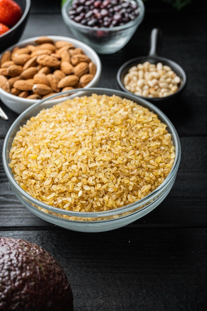 Bulgur grain in bowl, on black wooden background.