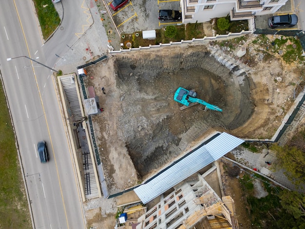 A bulldozer is digging a pit for the construction of another building in the middle of the city aerial view