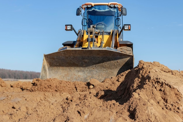 Bulldozer or loader moves the earth at the construction site against the blue sky An earthmoving machine is leveling the site Construction heavy equipment for earthworks