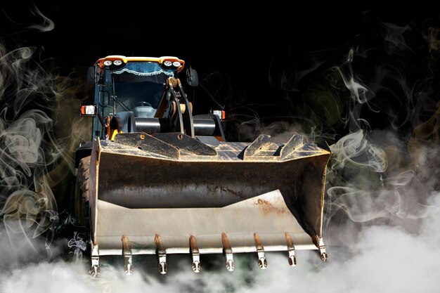 Bulldozer or loader in smoke on a dark background Powerful wheel loader or bulldozer with a large bucket Rental of construction equipment