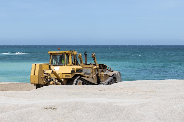 Bulldozer working to spread sand on a beach and sea at background