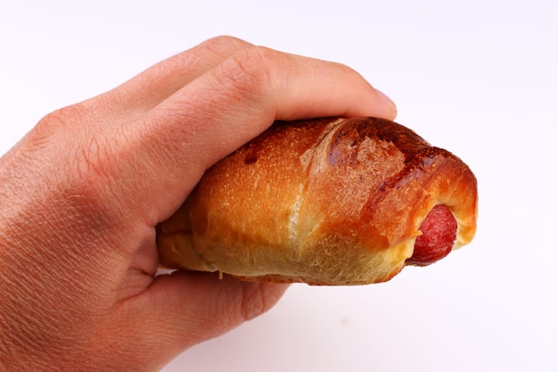 Bun with sausage in hand on a white surface