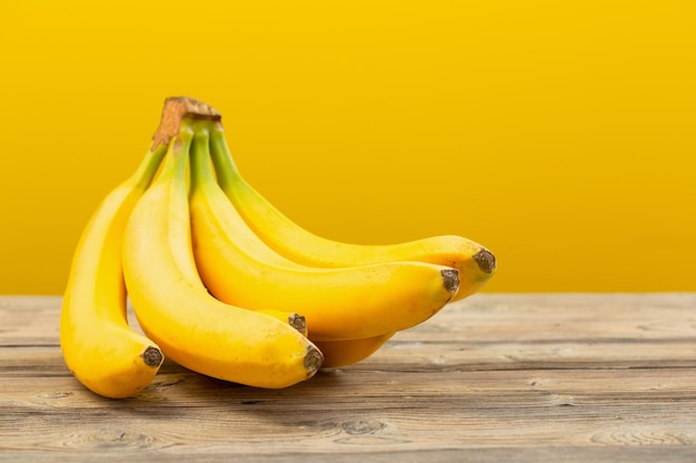 Bunch of bananas on wooden table on yellow background