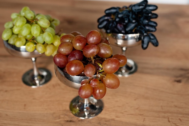 A bunch of blue green and red grapes in metal bowls on a wooden table Food healthy eating Soft selective focus