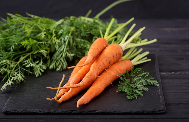 Bunch of fresh carrots with green leaves on  dark  wooden .