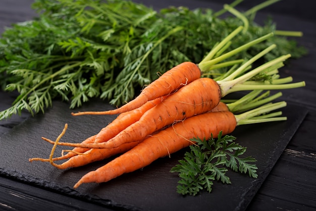 Bunch of fresh carrots with green leaves on wooden background