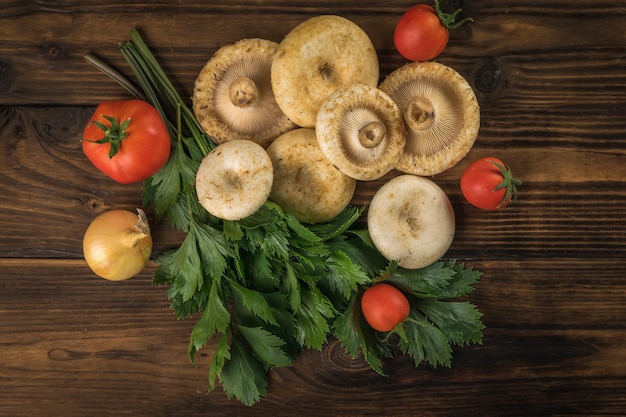 A bunch of fresh dairy wild mushrooms tomatoes and parsley on a wooden background Flat lay