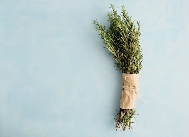 Photo bunch of fresh green twigs of rosemary wrapped in paper and tied with a rope lies on a blue background.