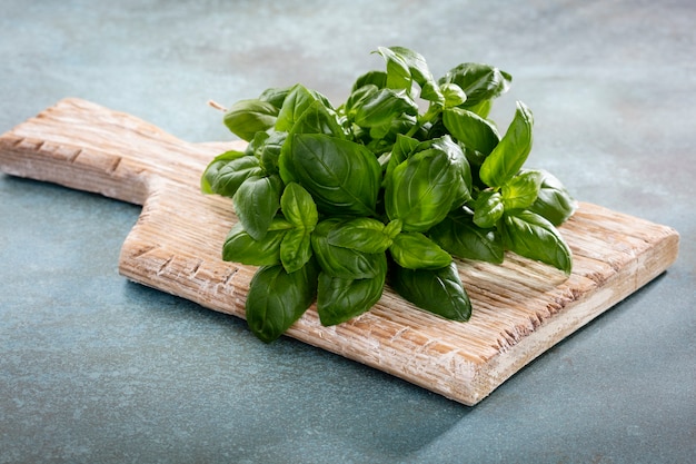 Bunch of fresh organic basil in cutting board on rustic wood